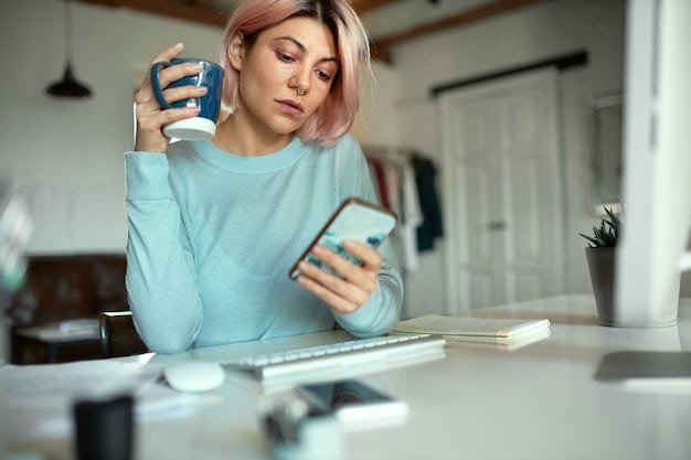 A person looking stressed while staring at a stack of bills on a wooden table, with a smartphone displaying a low bank balance notification in the background.